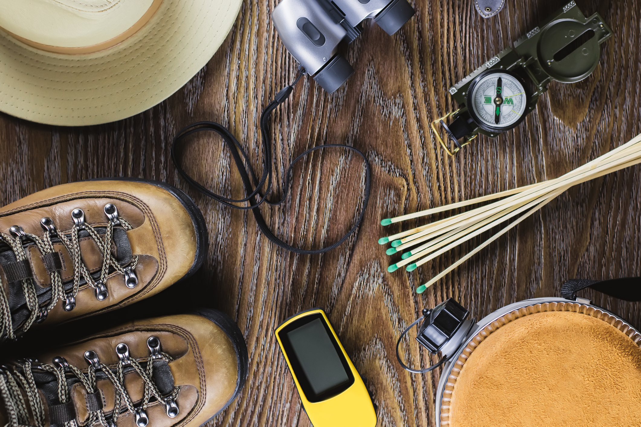 Hiking or travel equipment with boots, compass, binoculars, matches on wooden background. Active lifestyle concept.