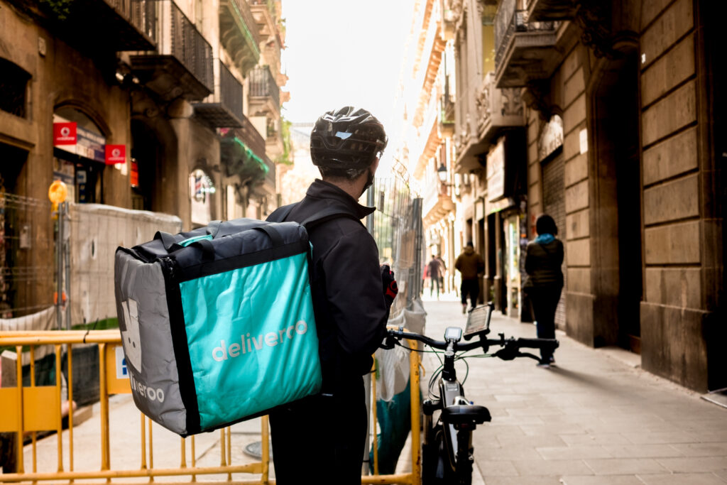 young Deliveroo delivey service company by bike in the streets of city working during the day