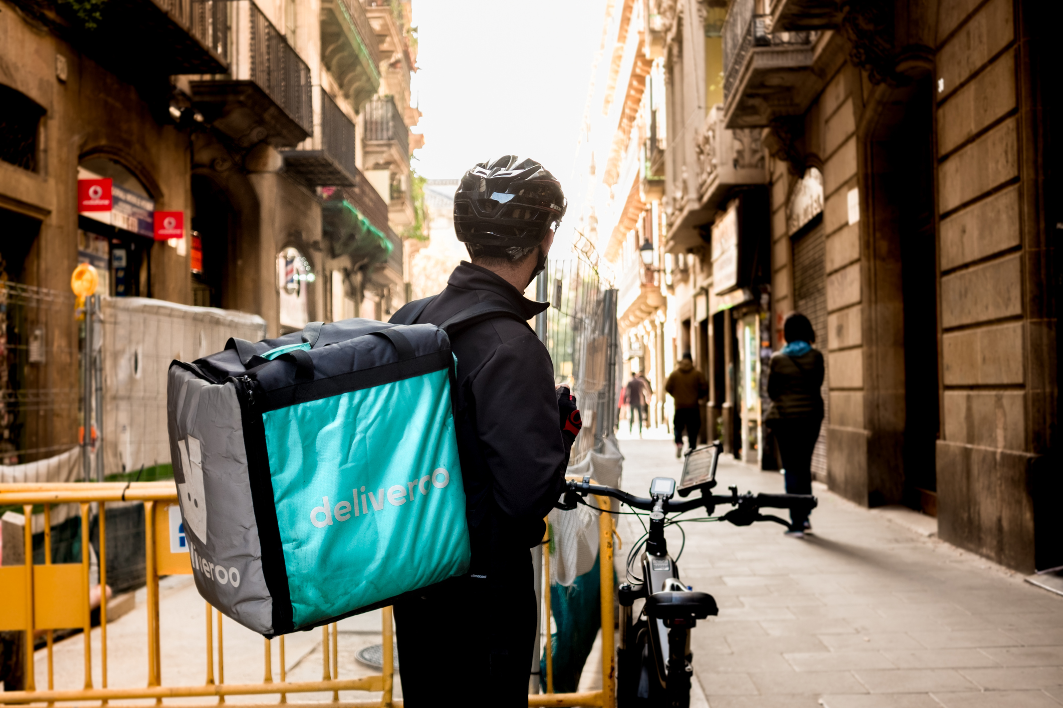 young Deliveroo delivey service company by bike in the streets of city working during the day
