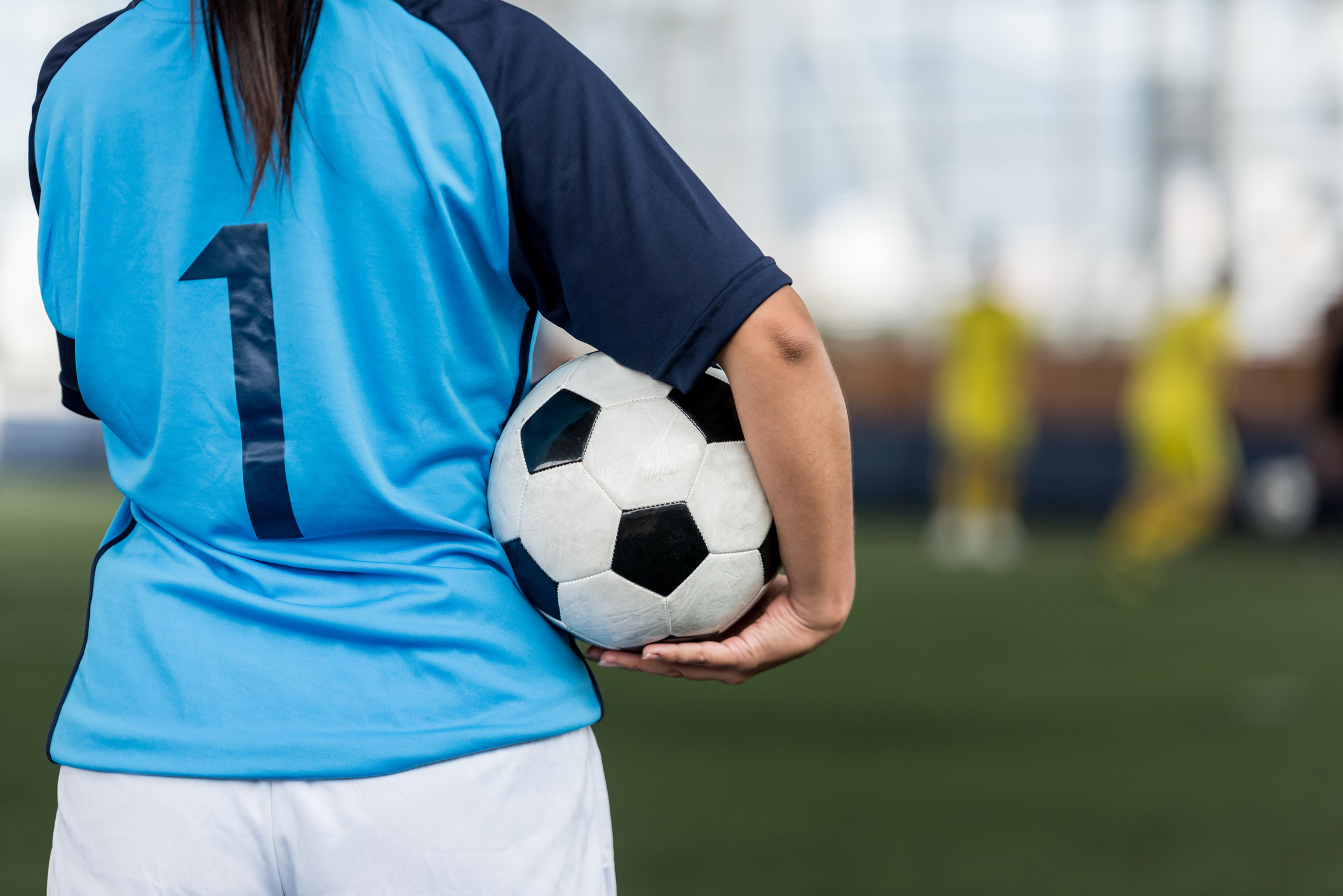 Unrecognizable female soccer player showing the back of her shirt and holding the soccer ball