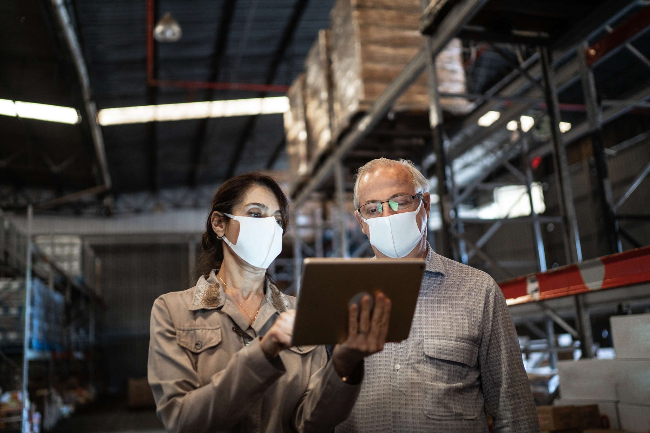 Senior partners walking and using digital tablet at warehouse - with face mask