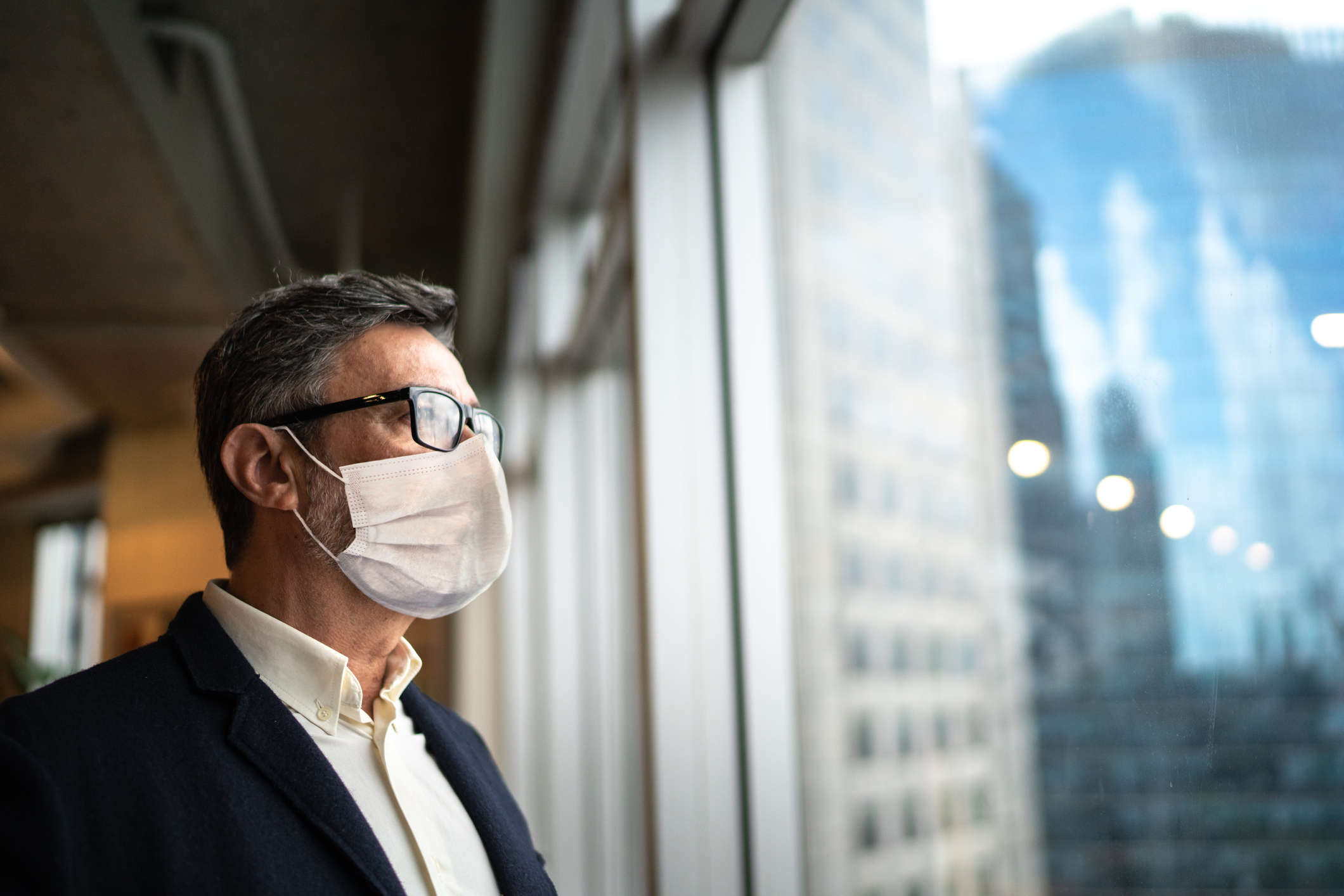 Mature businessman looking out of window with face mask