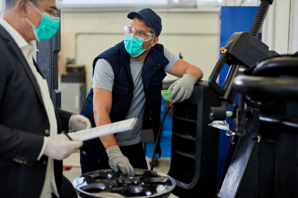 Auto repairman and his manager wearing protective face masks while talking in a workshop.