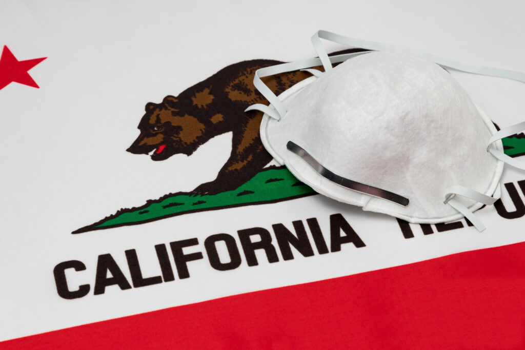California state flag and N95 face mask. Concept of state and local government face covering mandate, order, requirement and social distancing during Covid-19 coronavirus pandemic