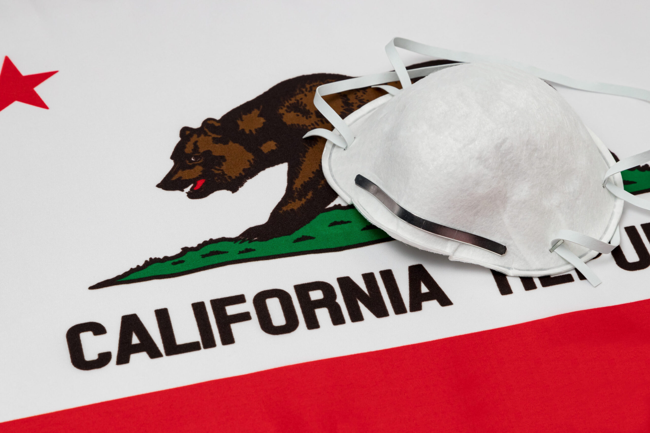 California state flag and N95 face mask. Concept of state and local government face covering mandate, order, requirement and social distancing during Covid-19 coronavirus pandemic