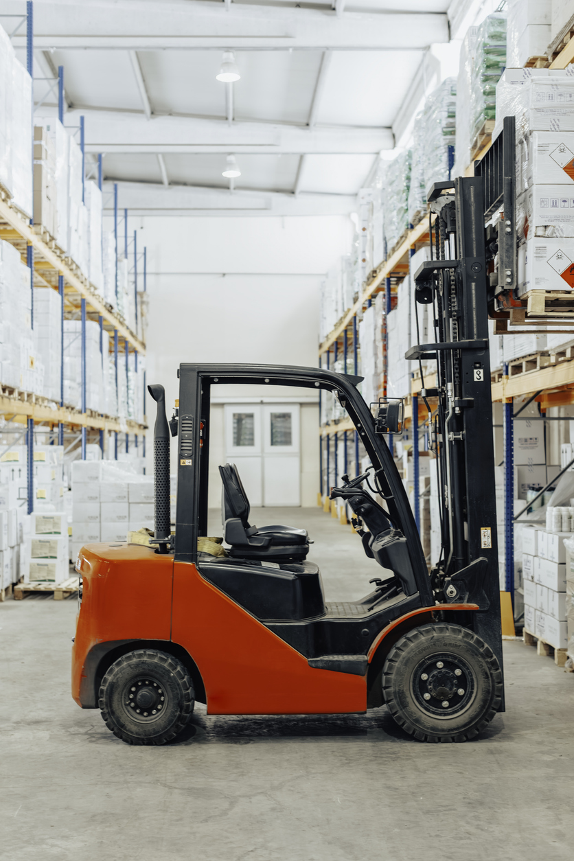Forklift vehicle parked inside organized warehouse aisle filled with stacked boxes and goods. KPA safety software