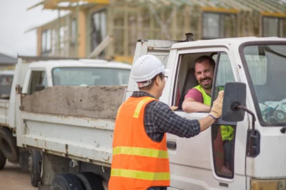Site worker in a hard hat and safety vest checking in a contractor driver at a construction site